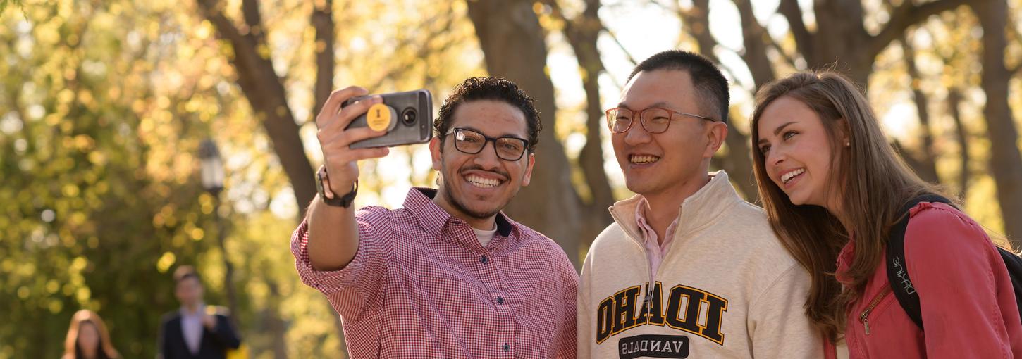 A student takes a selfie with two friends on the Administration Lawn.